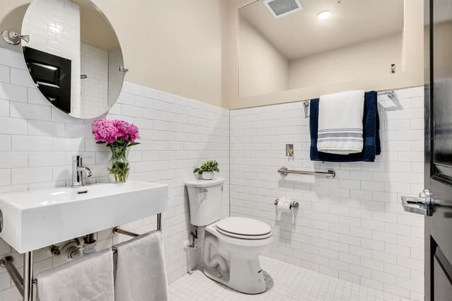 A white subway-tiled bath with a console sink, a round mirror, and a grab bar beside the toilet