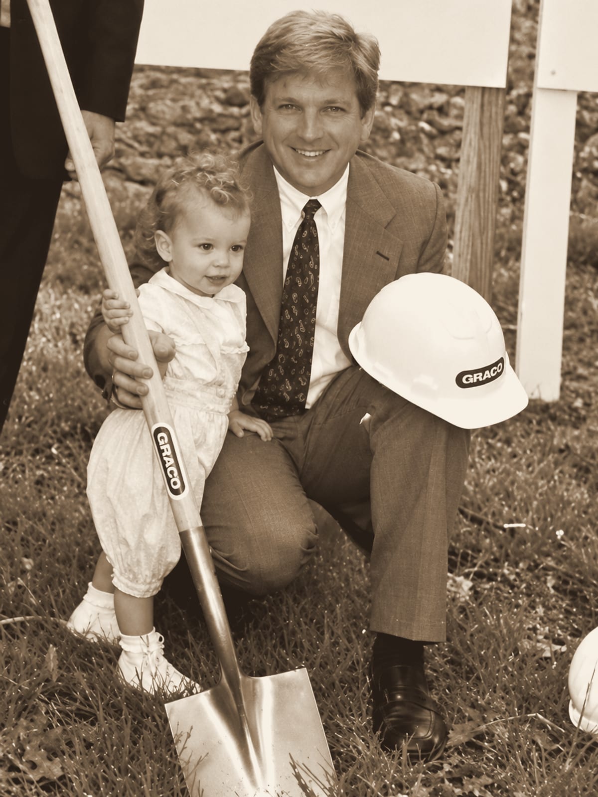Jeff Stephenson kneels with his young son beside a gold groundbreaking shovel